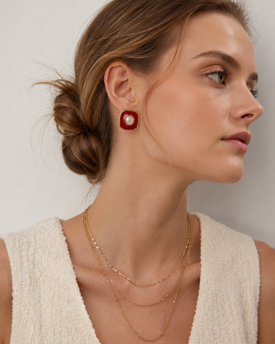Close-up of a European model wearing red enamel stud earrings with natural shell accents and intricate gold-tone detailing.