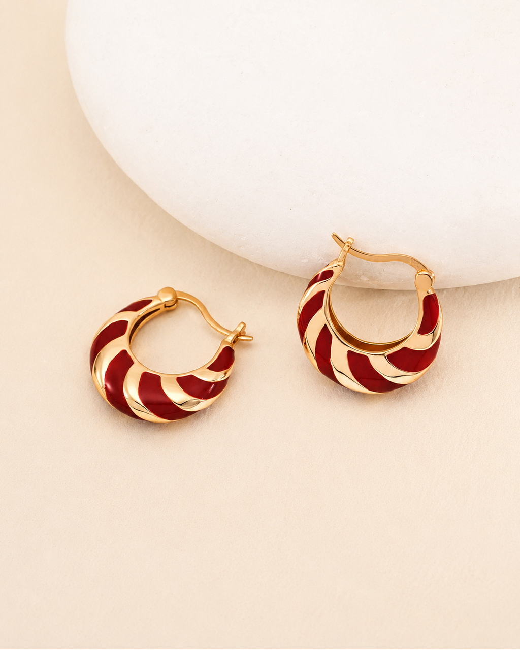 Red enamel and 18K gold plated hoop earrings styled beside a sculptural white display, showcasing their vintage-inspired design.