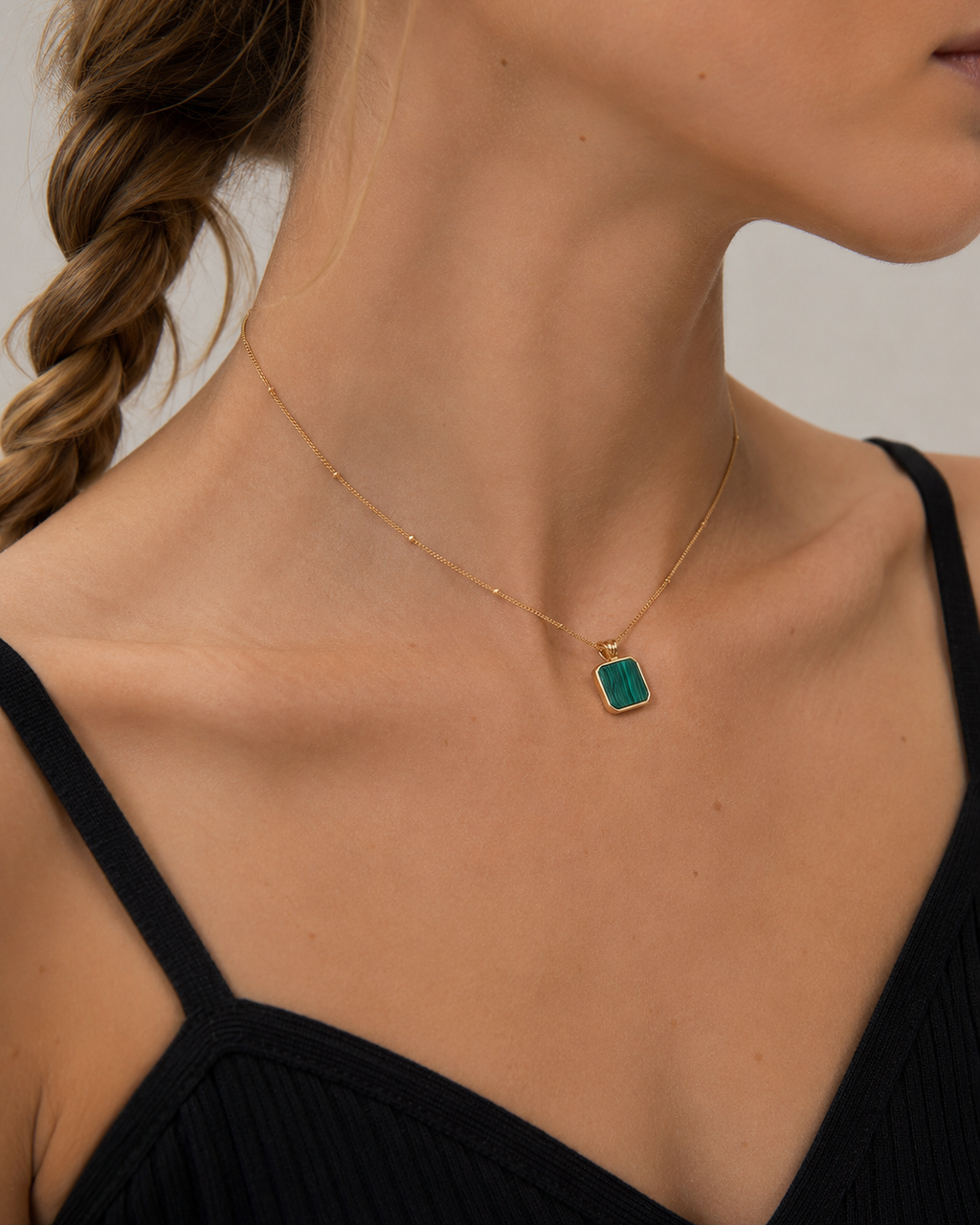 Female model wearing a square natural malachite pendant necklace in thick 18K gold plated sterling silver, styled with a minimalist black dress.