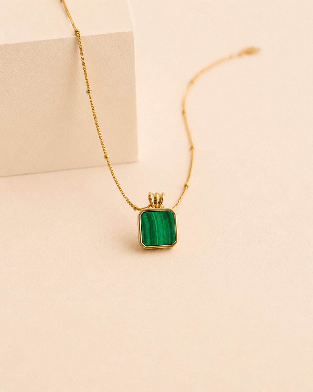 Square natural malachite pendant necklace in thick 18K gold plated sterling silver with adjustable chain on a soft cream background.