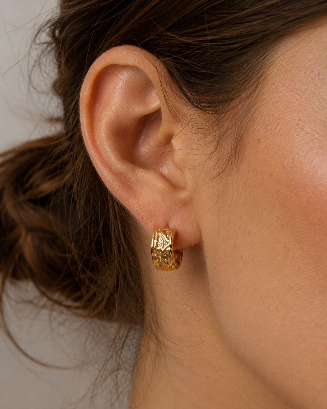 Close-up of a model wearing vintage carved huggie hoop earrings in thick 18K gold plated S925 sterling silver featuring an engraved texture.